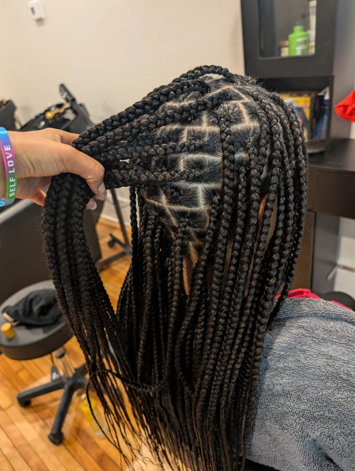 A stylist at Afro Royal Tresses demonstrating tension-free installation on long, dark box braids to protect the client's natural hair health.