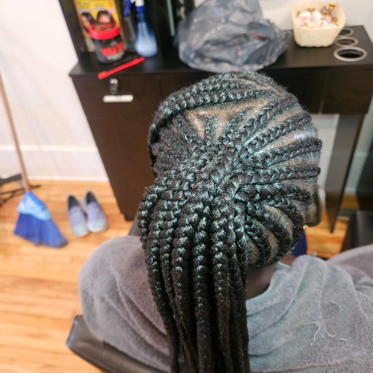 Back view of sleek, dark feed-in cornrows gathered into a long braided ponytail, providing a long-lasting protective style.