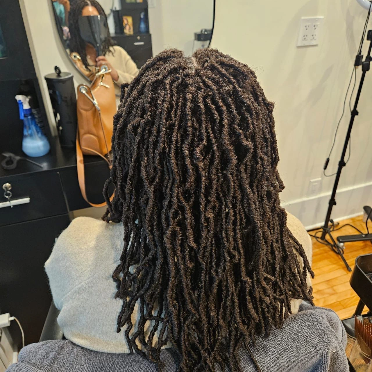 Shoulder-length dark faux locs freshly installed on a client seated in our premium Kitchener hair salon, showcasing our specialized loc care.