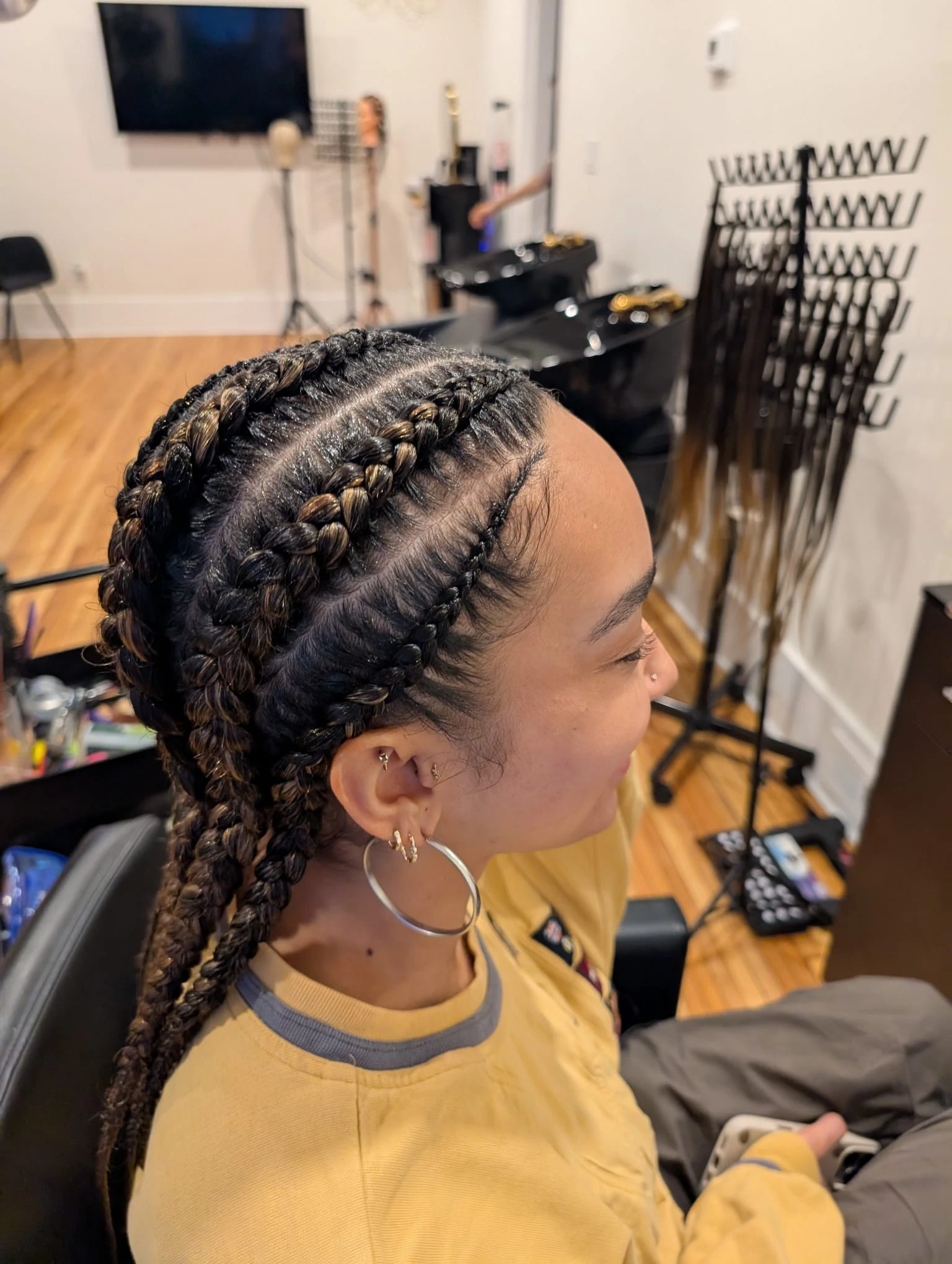 Side view of a smiling client with thick feed-in cornrows featuring blonde highlights, styled by Afro hair specialists in a luxury salon environment.