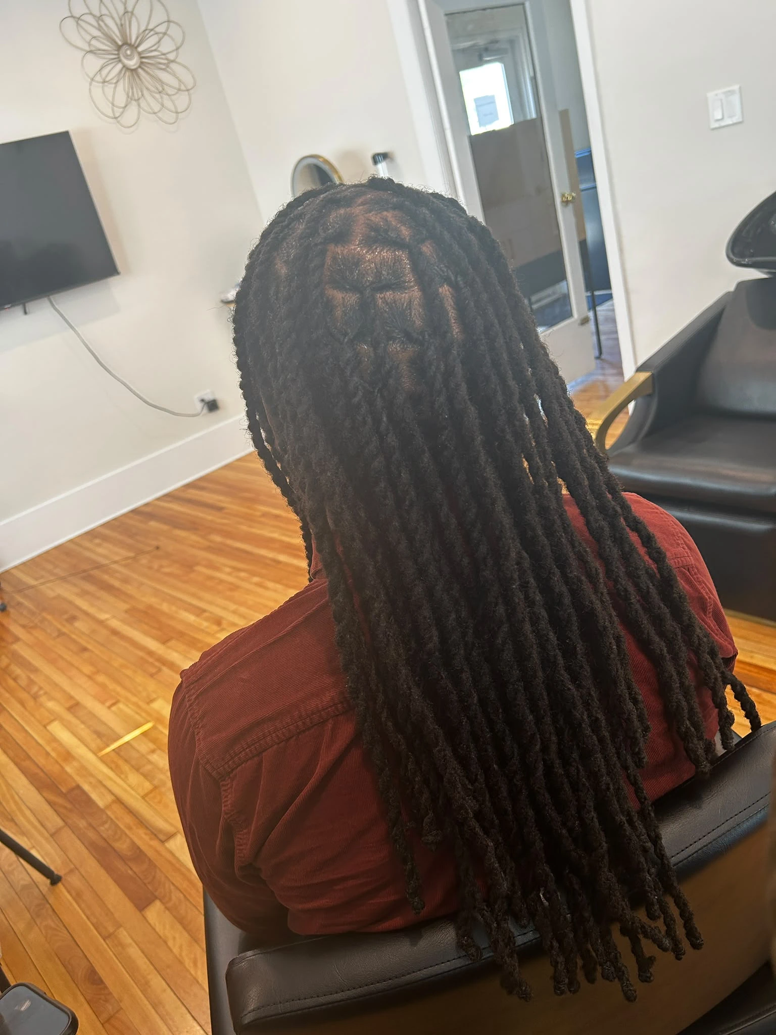 Back view of a client with long, freshly maintained locs, showcasing our specialized loc repair and natural hair care services.